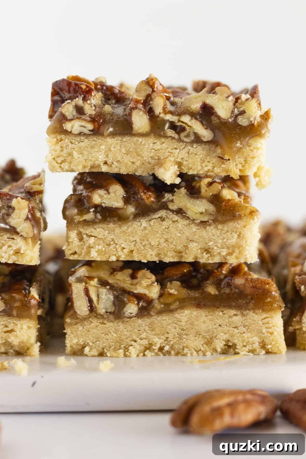 Buttery Pecan Shortbread Bars 2 Pecan Shortbread Bars stacked on top of each other on a white plate, showcasing their golden crust and rich pecan topping.