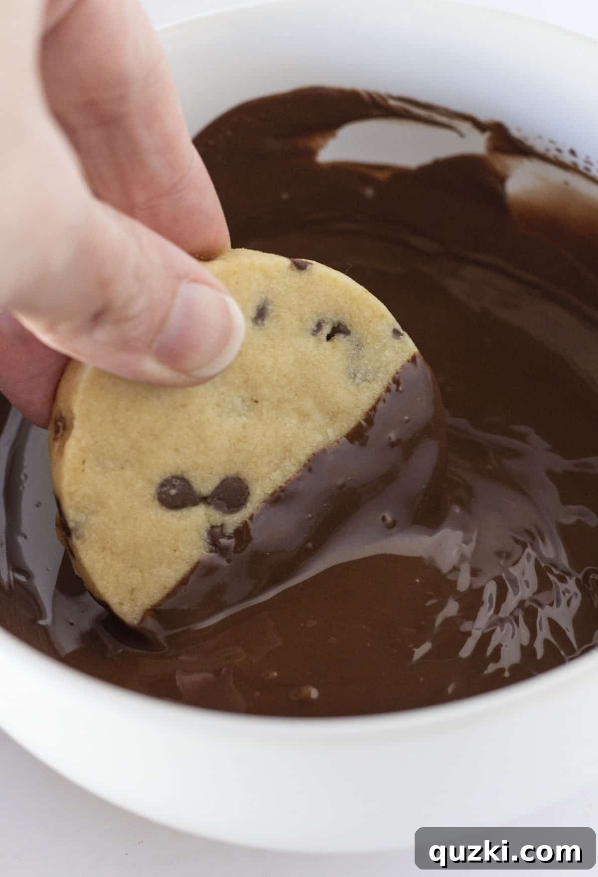 Detailed shot of the dipping process, showing a shortbread cookie halfway submerged in rich, melted chocolate, with a smooth coating.