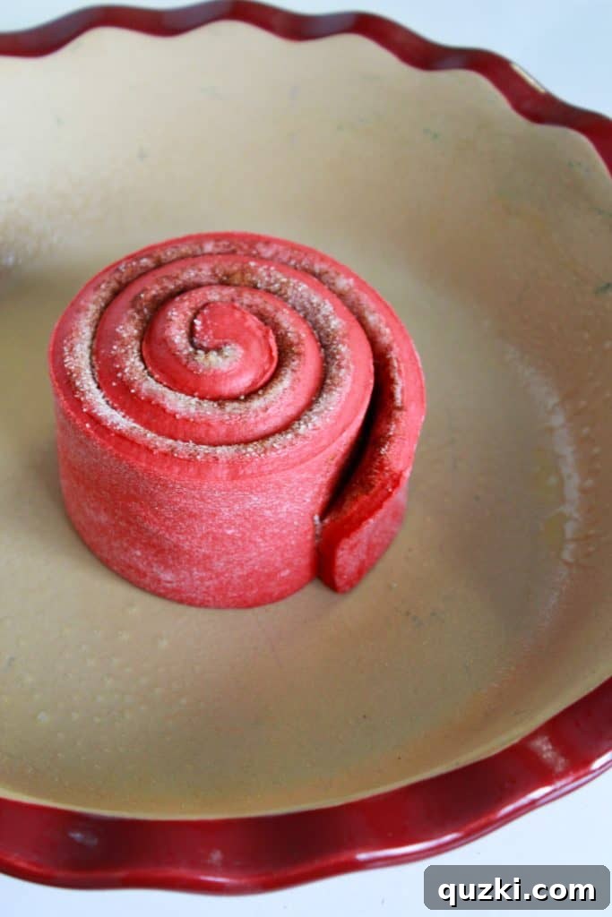 The initial stages of assembling the giant red velvet cinnamon roll cake, with the first dough strip forming a central spiral in a pie plate.
