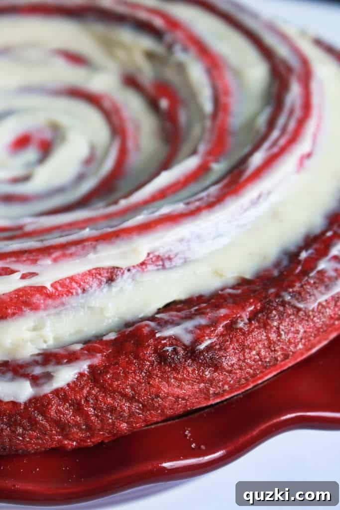Warm Red Velvet Cinnamon Roll Cake generously covered with a smooth, luscious cream cheese frosting, ready to be enjoyed.