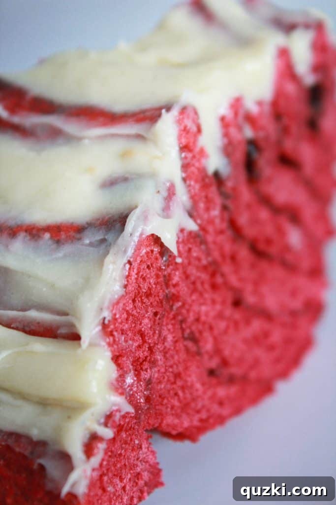 A perfectly sliced piece of Red Velvet Cinnamon Roll Cake, showcasing its vibrant red layers, cinnamon swirl, and thick cream cheese frosting.