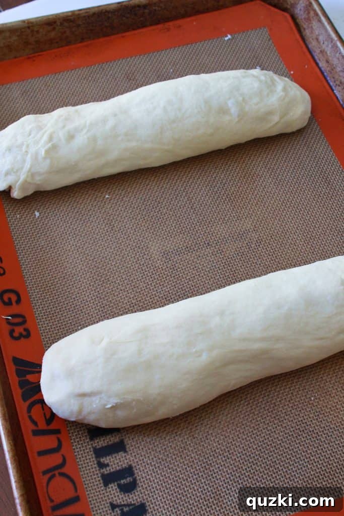 Shaping the French bread dough into two elegant, elongated loaves on a baking sheet, ready for scoring and proofing.
