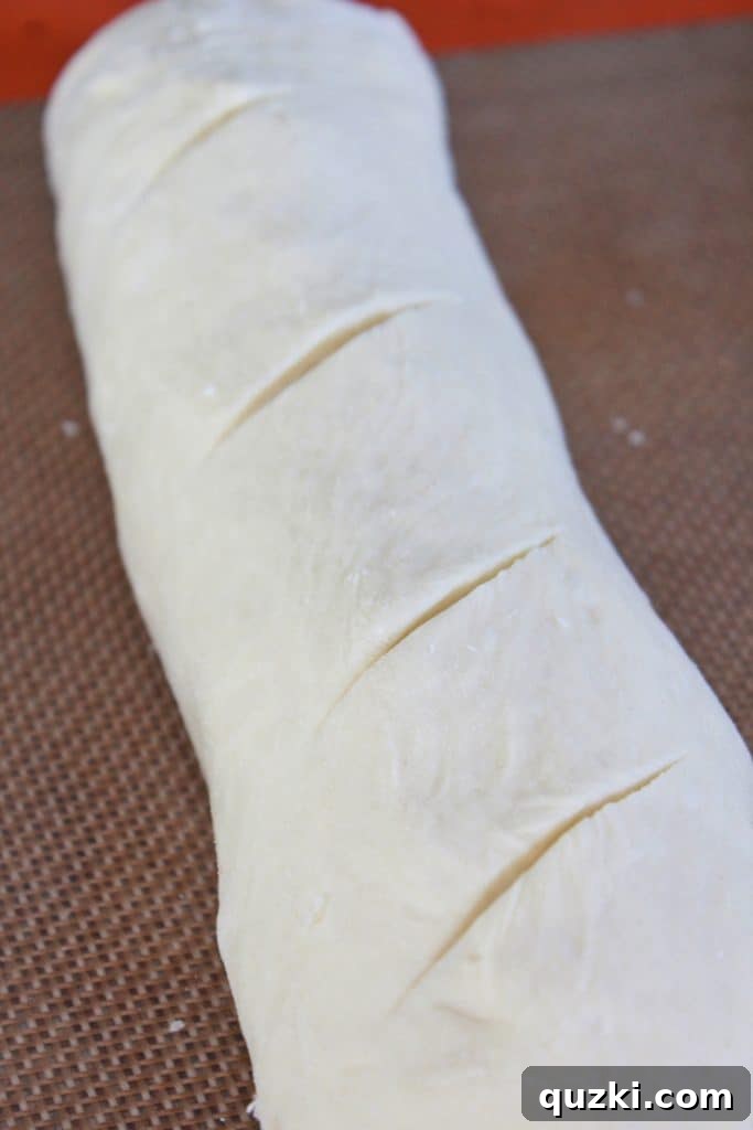 Scoring diagonal slits on top of French bread dough with a sharp knife, a crucial step for proper expansion and crust development.