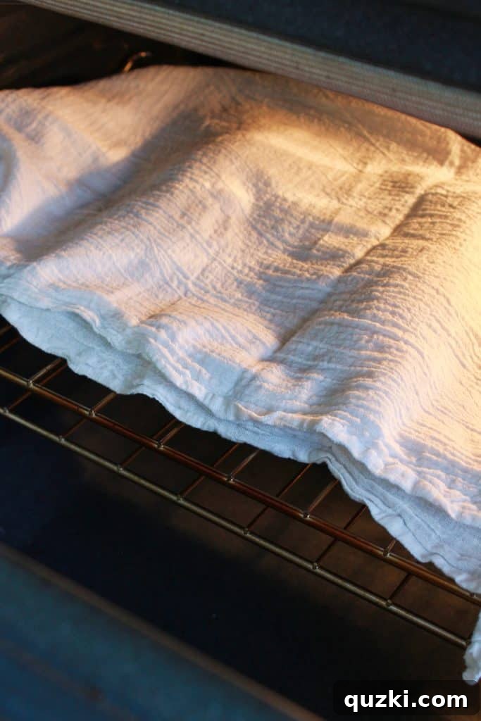 Two loaves of French bread dough, covered with a towel, placed inside a warm oven to facilitate a quick rise.