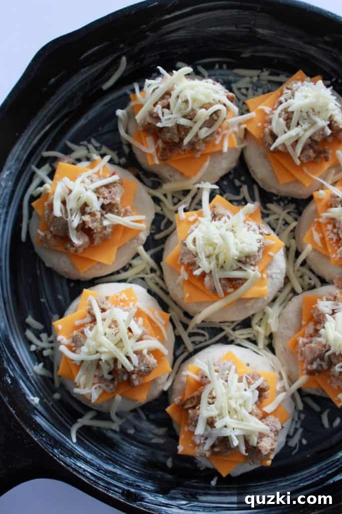 Shredded mozzarella cheese being sprinkled over the sausage and biscuits.