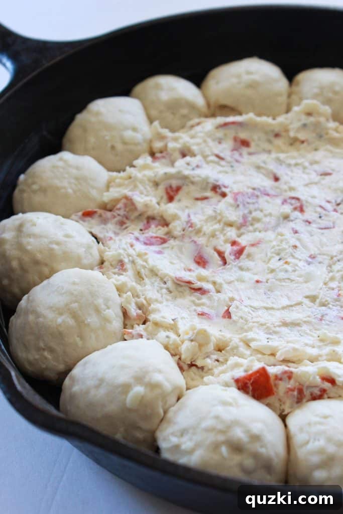 Creamy pepperoni pizza dip mixture evenly spread in the center of the skillet, surrounded by biscuit balls