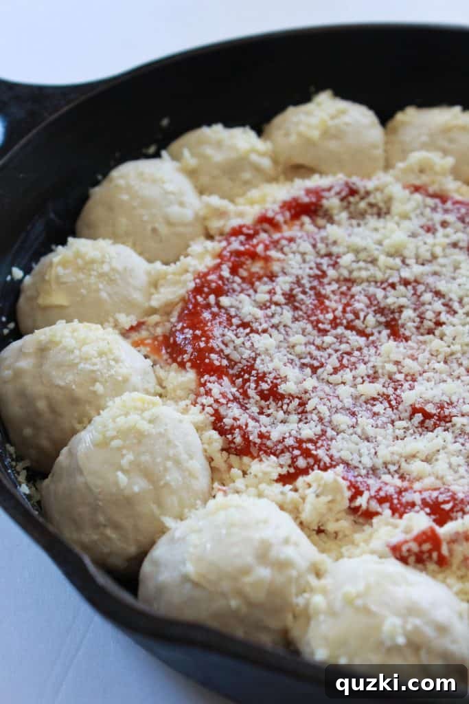 Pizza dip in skillet topped with pizza sauce and sprinkled generously with Parmesan cheese