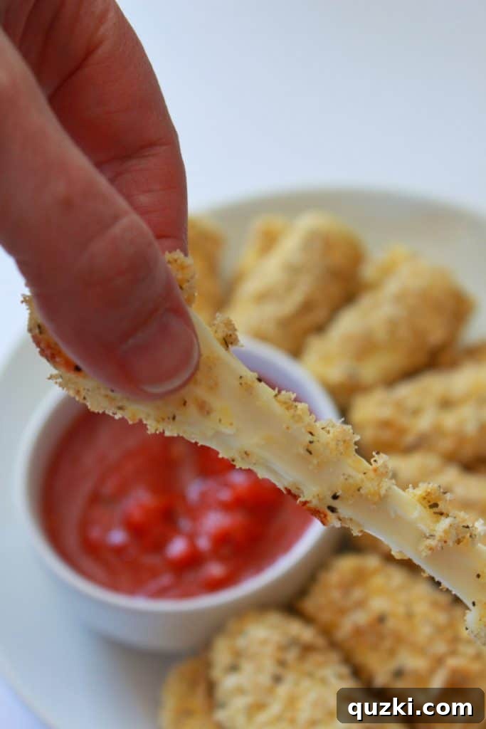 A baked mozzarella stick being pulled apart, showcasing a long, gooey strand of melted cheese.