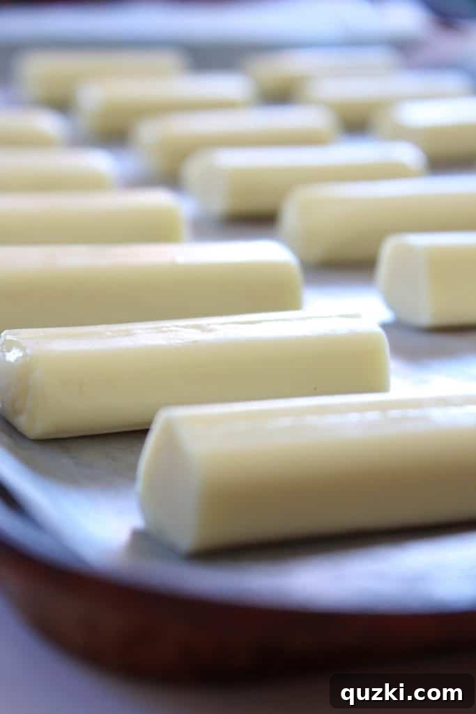 Mozzarella string cheese sticks cut in half and arranged on a parchment-lined baking sheet, ready for freezing.