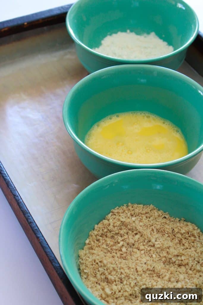 Three bowls set up as a dredging station: one with flour, one with whisked eggs, and one with seasoned panko breadcrumbs.