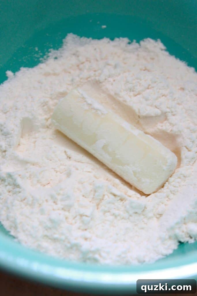 A hand dipping a half-cut mozzarella stick into a bowl of flour, ensuring an even coating.