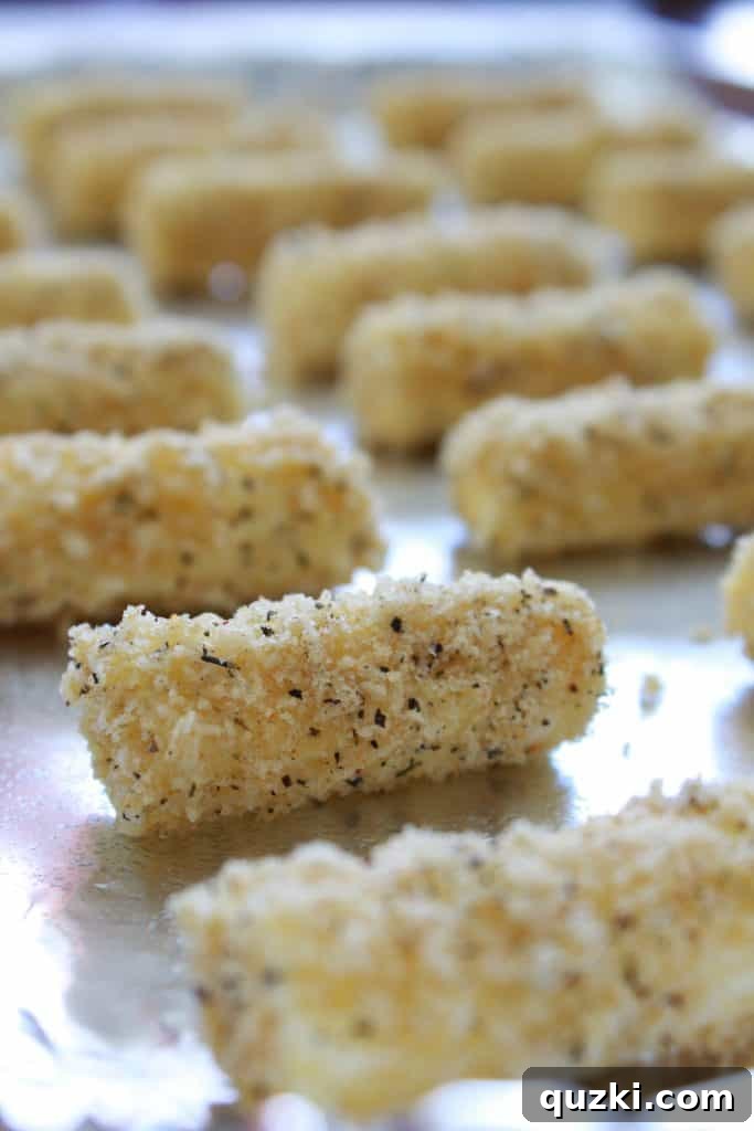 Coated mozzarella sticks arranged on a foil-lined baking sheet, ready for their second freeze.