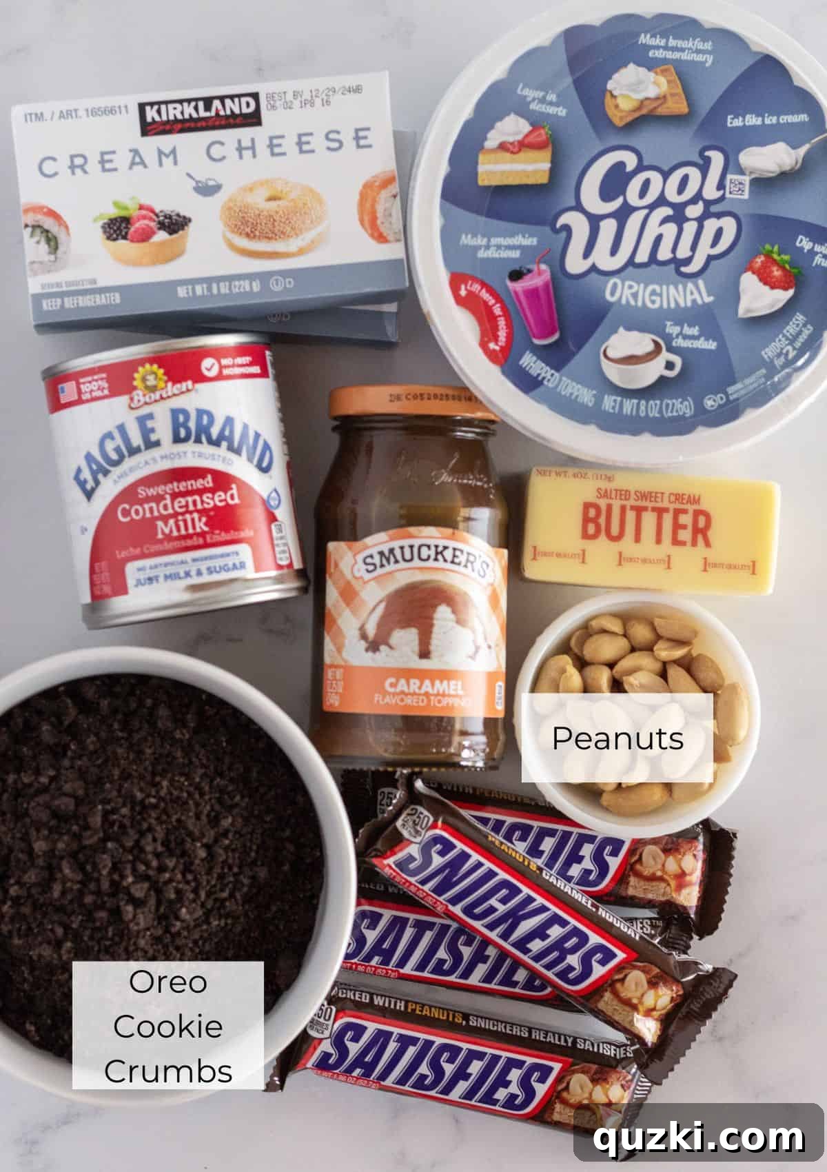 A vibrant, neatly arranged overhead shot of all the key ingredients required to assemble a decadent Snickers Cheesecake, including Oreo cookies, cream cheese, Snickers bars, and caramel sauce.