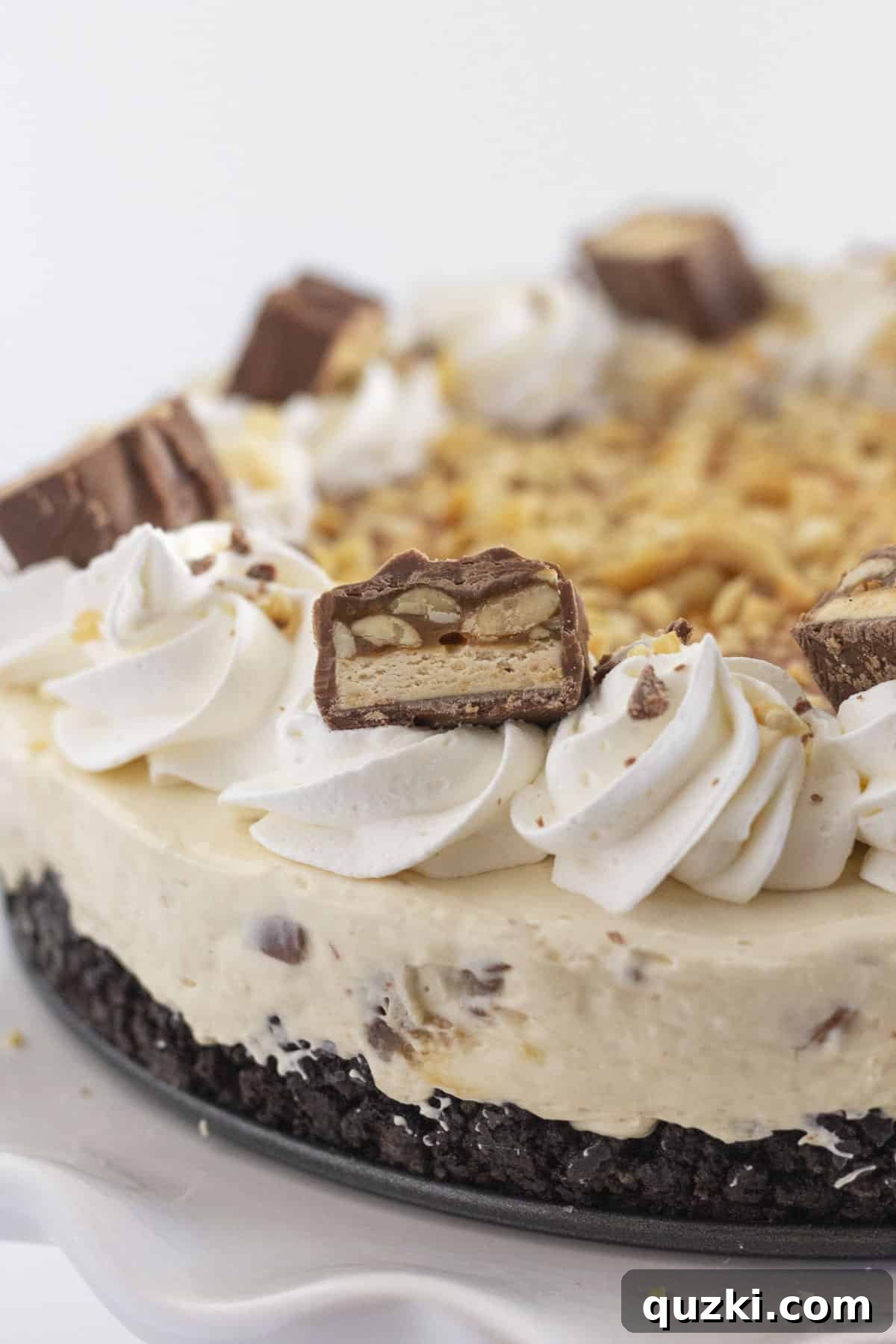 A stunning close-up of the finished Snickers no-bake cheesecake, elegantly garnished with generous drizzles of caramel sauce and a scattering of chopped, lightly salted peanuts, ready to be admired and enjoyed.