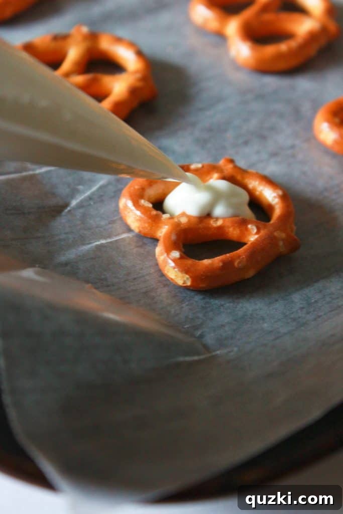 White Chocolate Dipped Pretzel Hearts 4 Melted white chocolate being carefully piped into the heart-shaped center of mini pretzels using a piping bag, demonstrating precision.