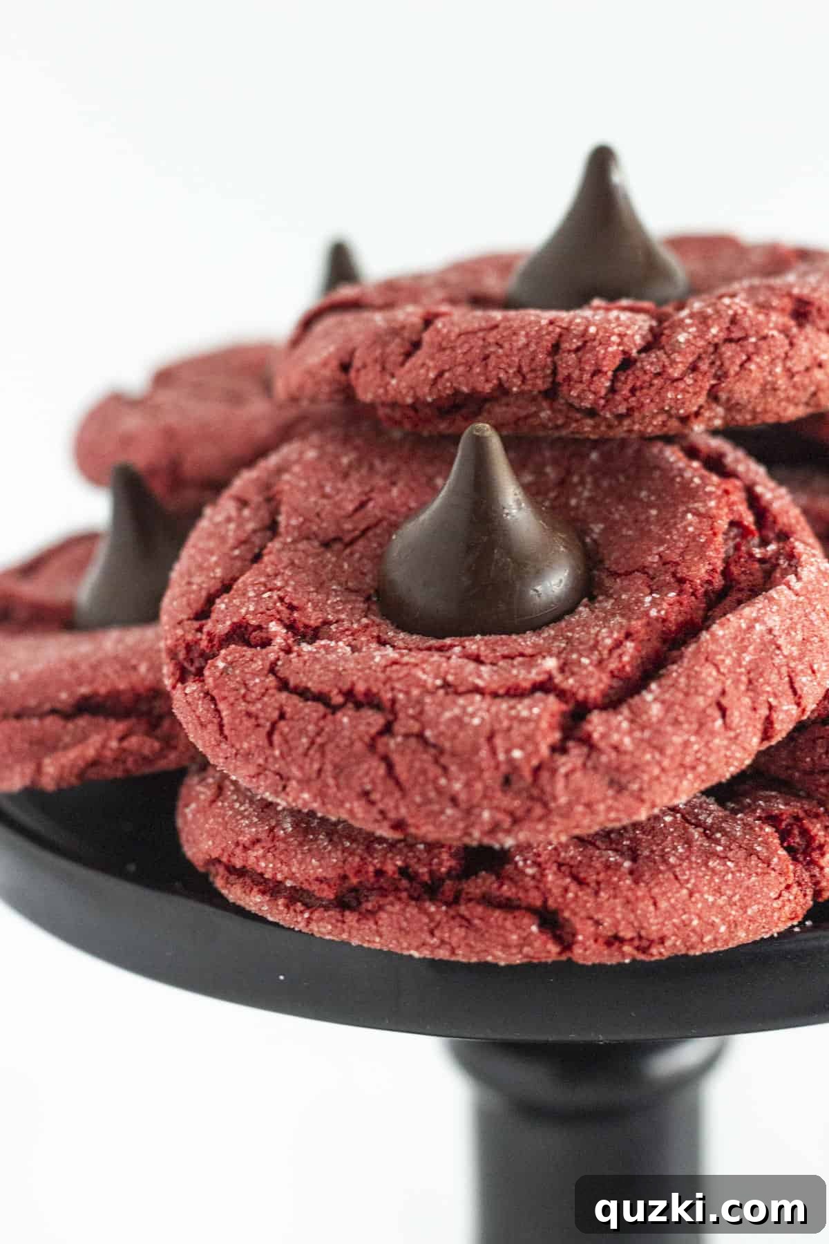 Effortless Red Velvet Kiss Cookies 6 Red Velvet Kiss cookies beautifully arranged on a black cake plate, showcasing their vibrant color and chocolate tops.