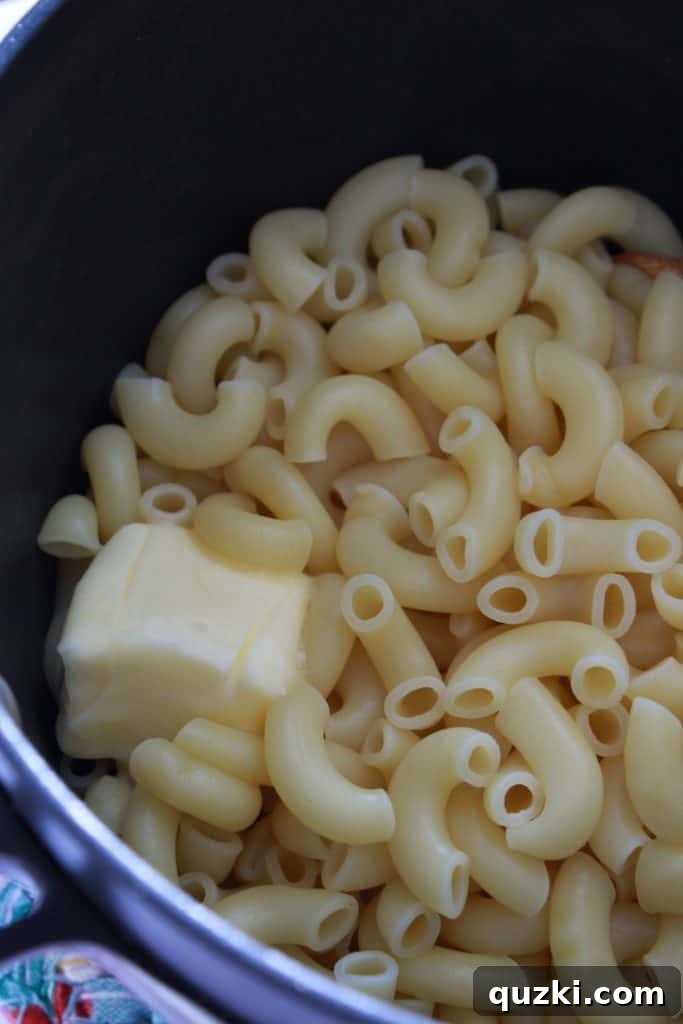 Classic Homemade Macaroni and Cheese 4 Adding pats of butter to the freshly cooked and drained pasta in a saucepan, preparing it for the cheese sauce.