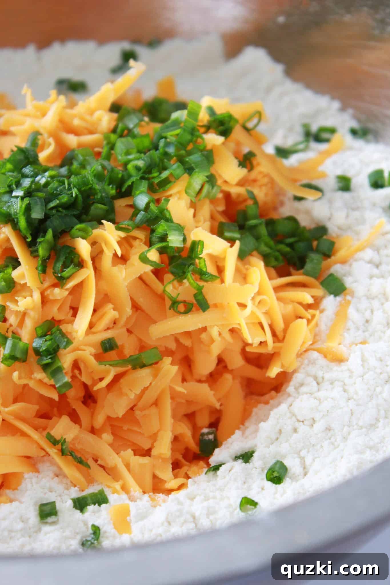Combining the dry ingredients with generous amounts of shredded cheddar cheese and fresh, chopped chives.