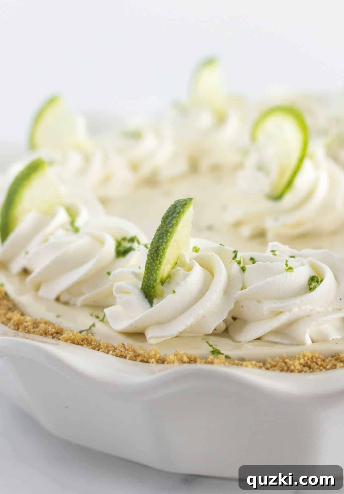 A key lime pie with homemade whipped cream and a graham cracker crust, garnished with lime slices.