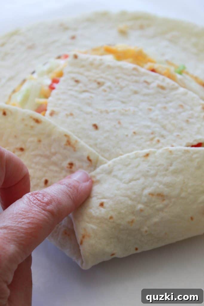 Golden Crunch Pocket 9 Step 6: Beginning to fold the edges of the large flour tortilla over the filling, covering the small tortilla piece in the center.