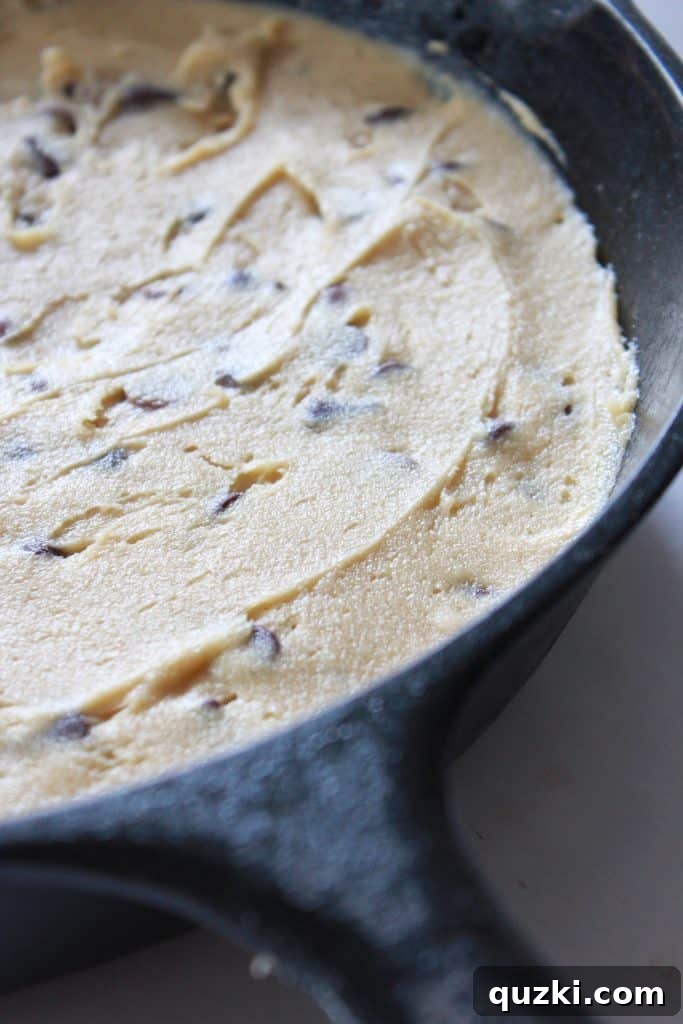 Decadent Skillet Chocolate Chip Cookie 8 Chocolate chip cookie dough spread evenly in a cast iron skillet, ready for baking