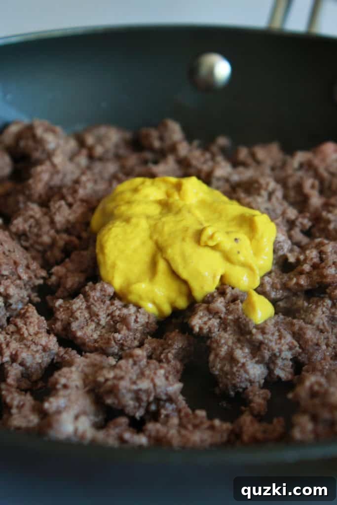Ground beef cooking in a skillet with yellow mustard
