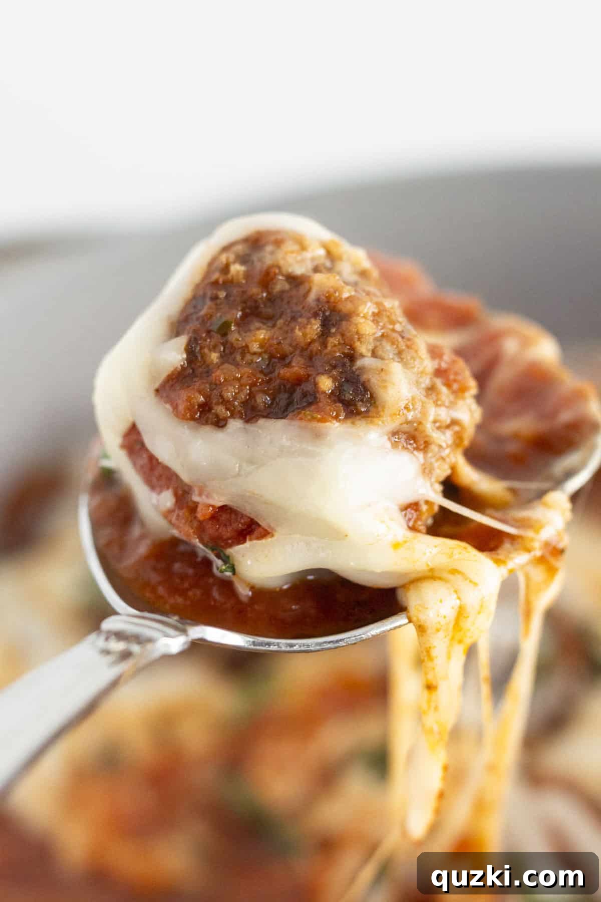 A single meatball on a spoon, lifted from the skillet, showcasing the deliciousness of the dish.