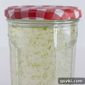 A close-up view of a glass jar filled with bright green lime simple syrup, garnished with fresh lime slices.