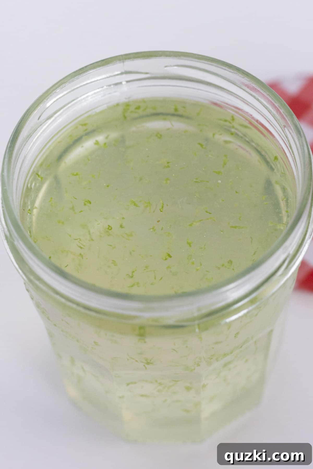 A top-down view looking into a glass jar filled with the clear, inviting lime simple syrup.