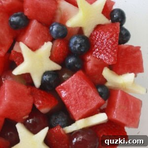 A bowl full of fourth of July fruit salad, garnished with mint leaves and glistening with simple syrup.