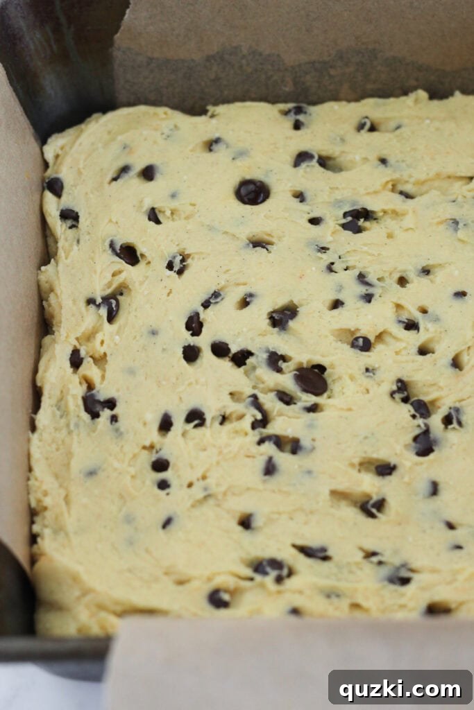 Pressing the cookie dough into a parchment-lined baking pan for an even layer.