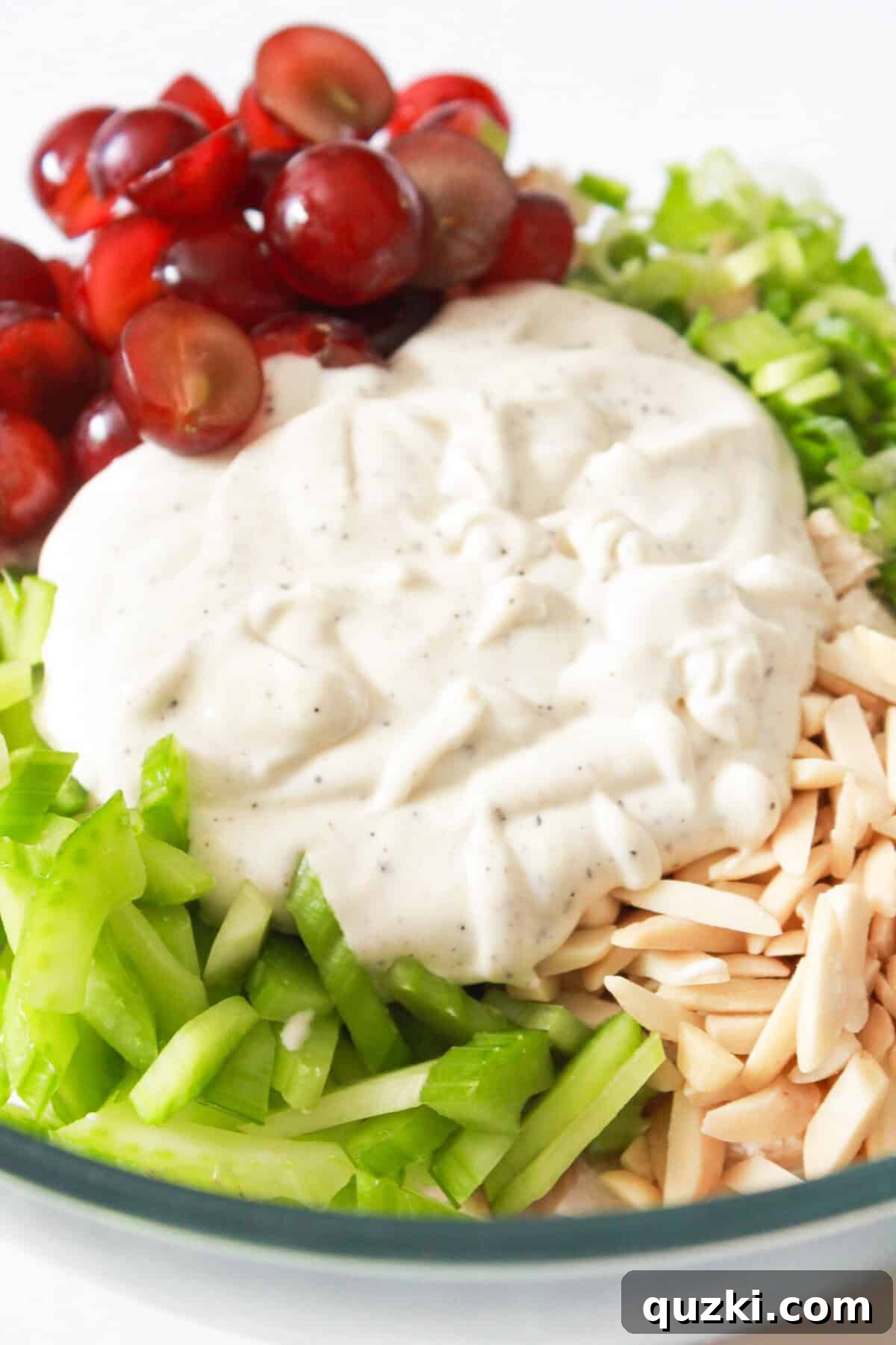 Pouring a creamy homemade dressing over the chicken salad with almonds and grapes.