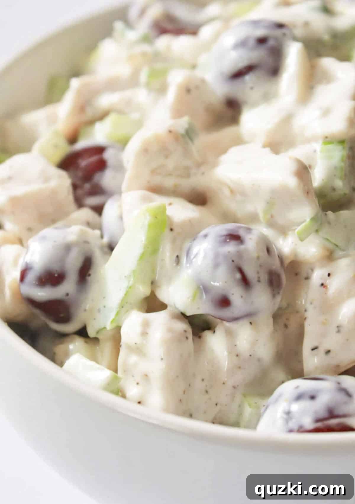 A pristine white bowl filled with creamy chicken salad, topped with fresh grapes and slivered almonds.