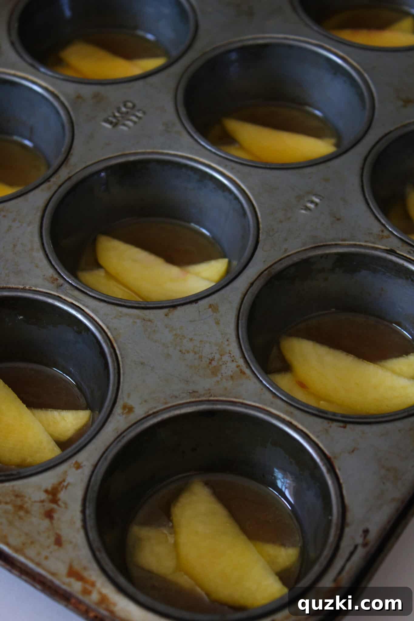 Effortless Peach Flip Cupcakes 5 Close-up of peach slices and brown sugar in a muffin tin, ready for cake batter.