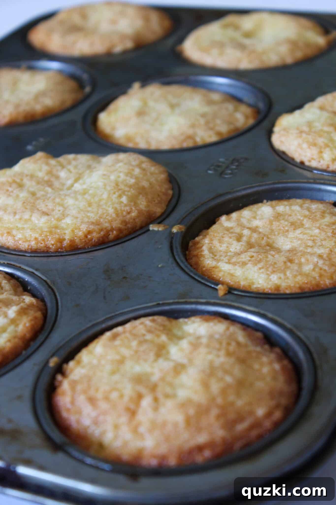 Effortless Peach Flip Cupcakes 9 Freshly baked peach upside-down cupcakes cooling in the muffin tin before inversion, with a knife used to loosen edges.