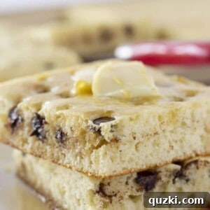 A close-up of a serving of sheet pan pancakes with chocolate chips and a drizzle of syrup, illustrating the delicious outcome.