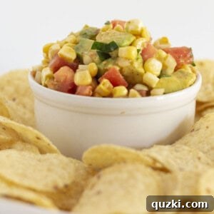 Fresh corn and avocado salsa, vibrant and ready to eat, served in a white bowl with a side of crispy corn chips.