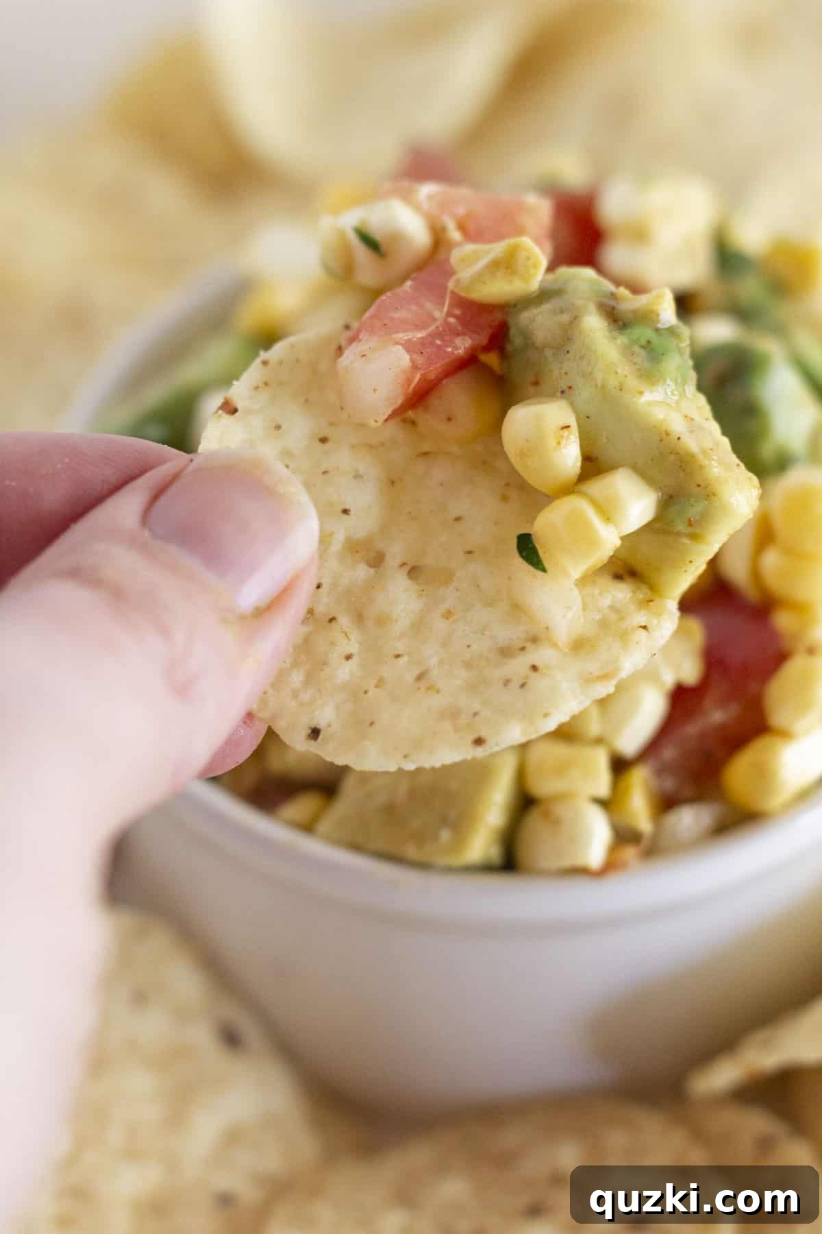 Vibrant Corn and Avocado Salsa 6 A corn chip being dipped into a bowl of fresh corn and avocado salsa, highlighting its vibrant textures and inviting taste.