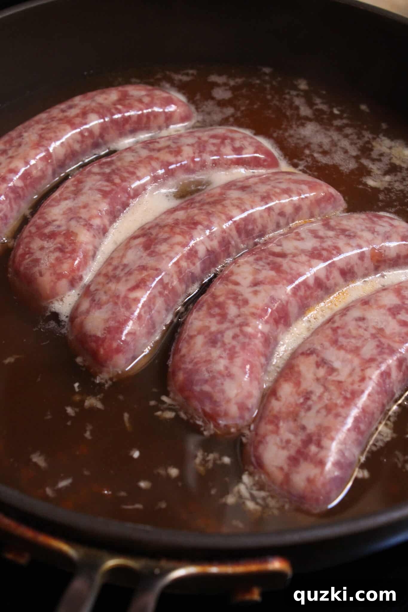 Tek Tepsi Sosisli Patates Lezzeti 5 Brats boiling in a skillet, absorbing rich flavors from the beef stock or beer.