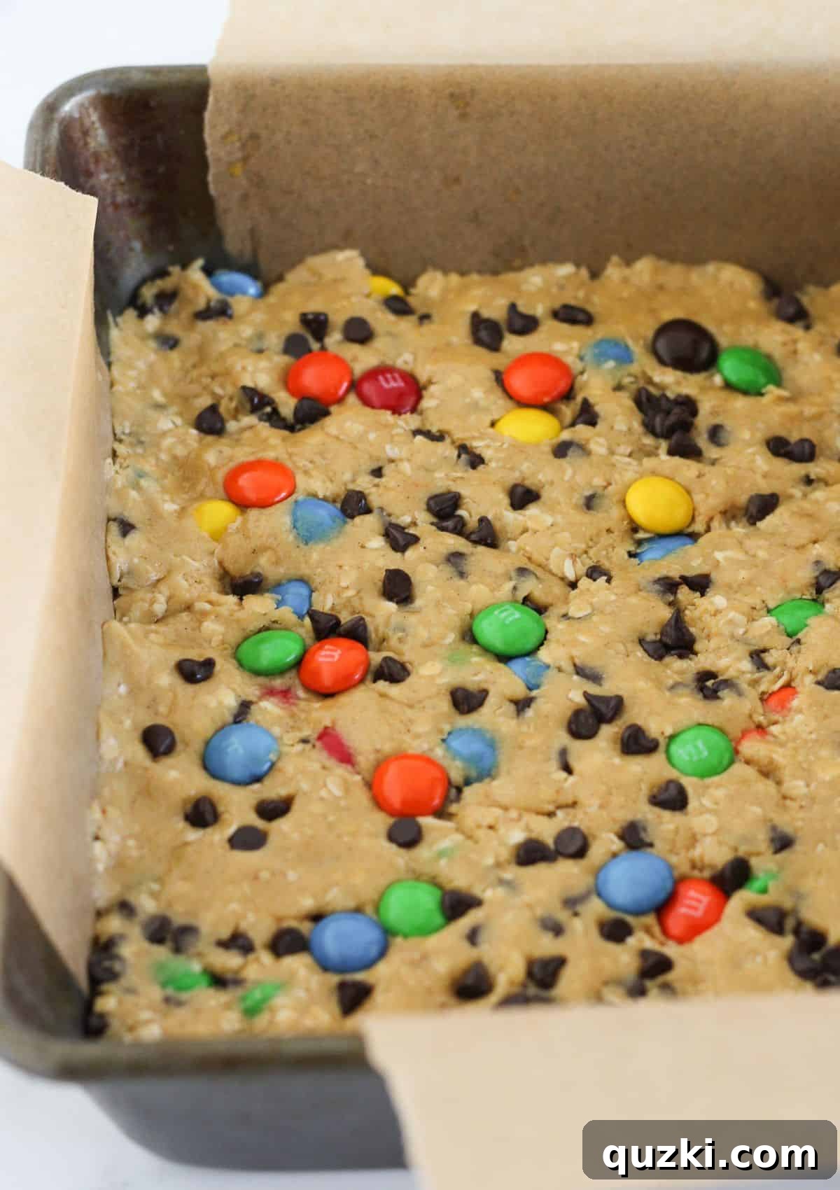 Spreading the dense monster cookie dough evenly into the prepared 9x9 inch baking pan.