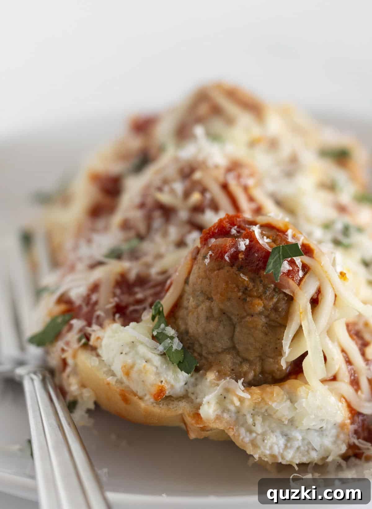 A delicious serving of Meatball Sub Casserole on a white plate with a silver fork, showcasing the layers of cheese, meatballs, and bread.