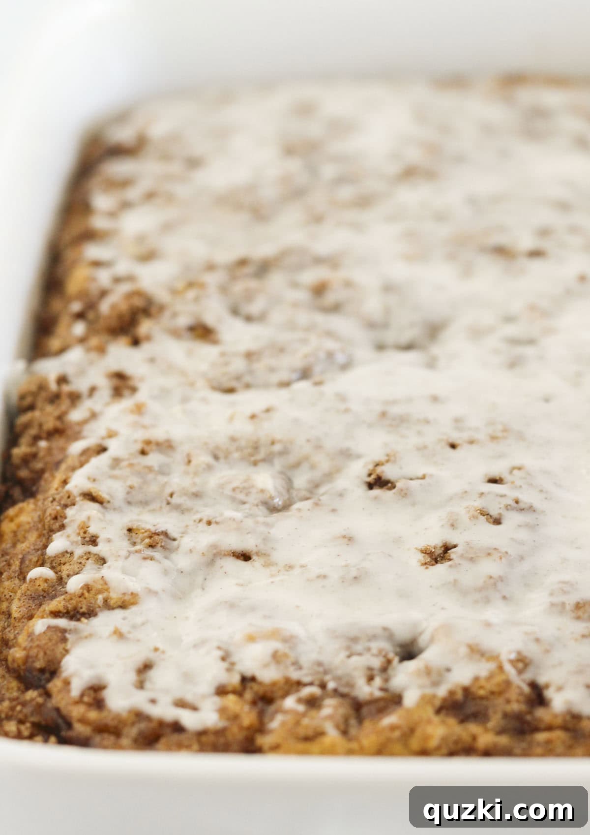 Applying a generous layer of delicious vanilla-pumpkin spiced glaze over the cooled pumpkin cinnamon roll cake.