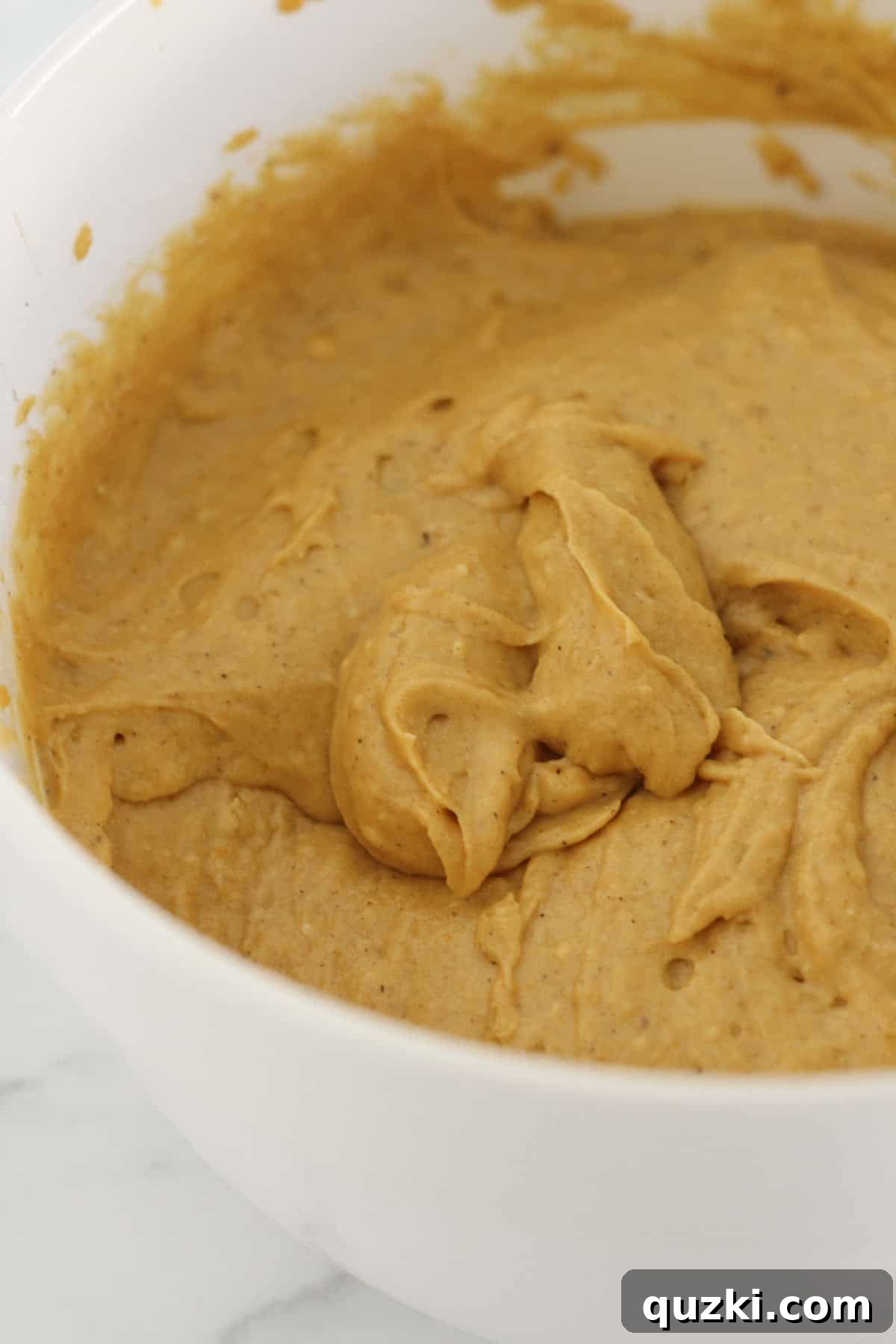 Adding pumpkin puree, eggs, and vegetable oil to the dry cake mix and stirring to form a smooth cake batter.