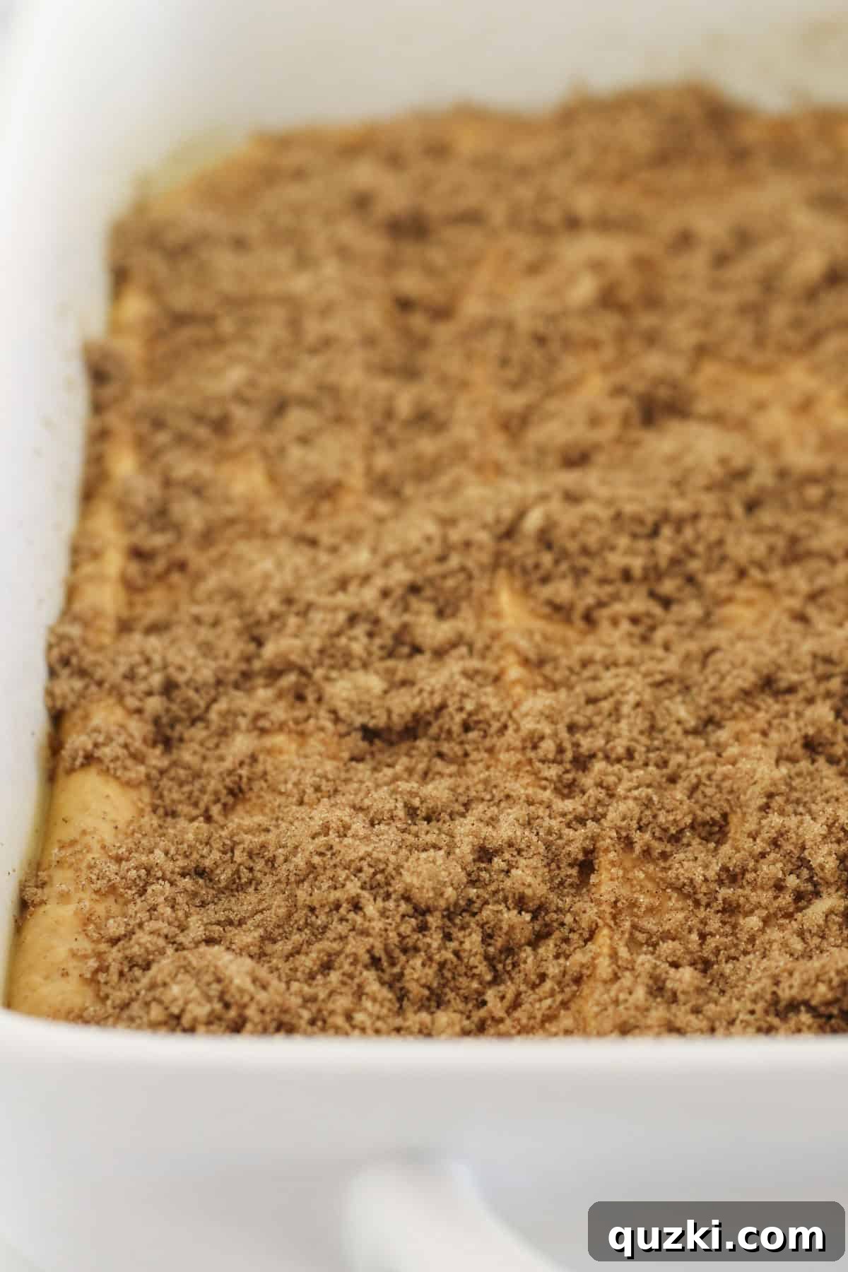 Adding the first half of the pumpkin cake batter to a prepared 9x13 baking pan, followed by half of the cinnamon swirl mixture.