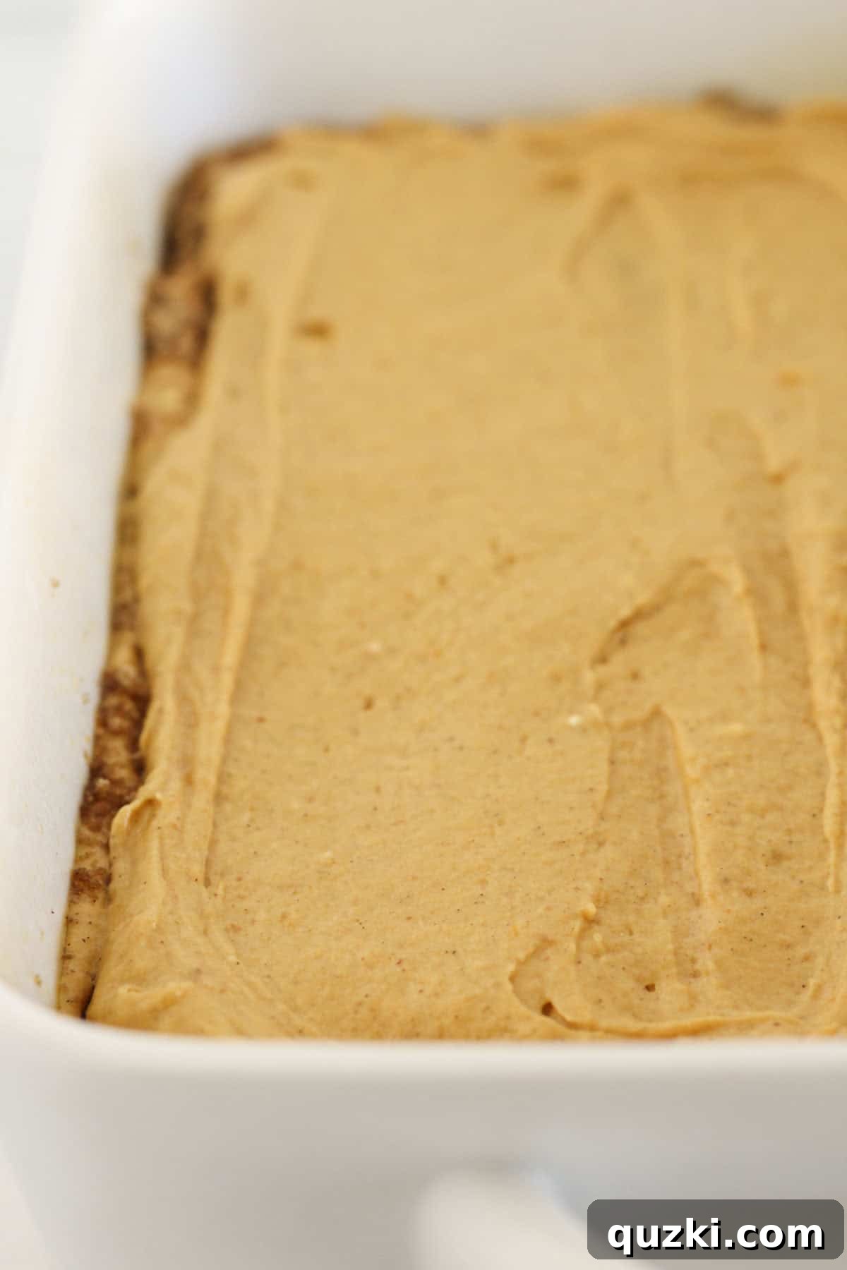 Carefully spreading the remaining pumpkin cake batter over the first cinnamon swirl layer, creating the second cake layer.