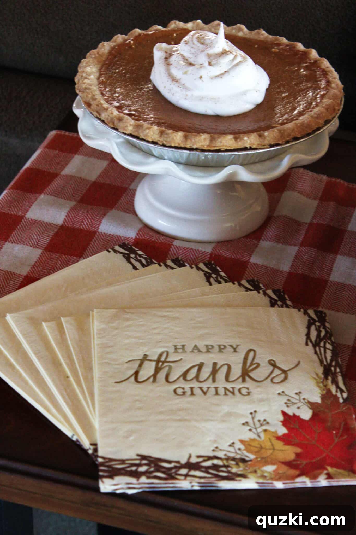 Classic pumpkin pie on a cake stand with whipped cream and Thanksgiving napkins.