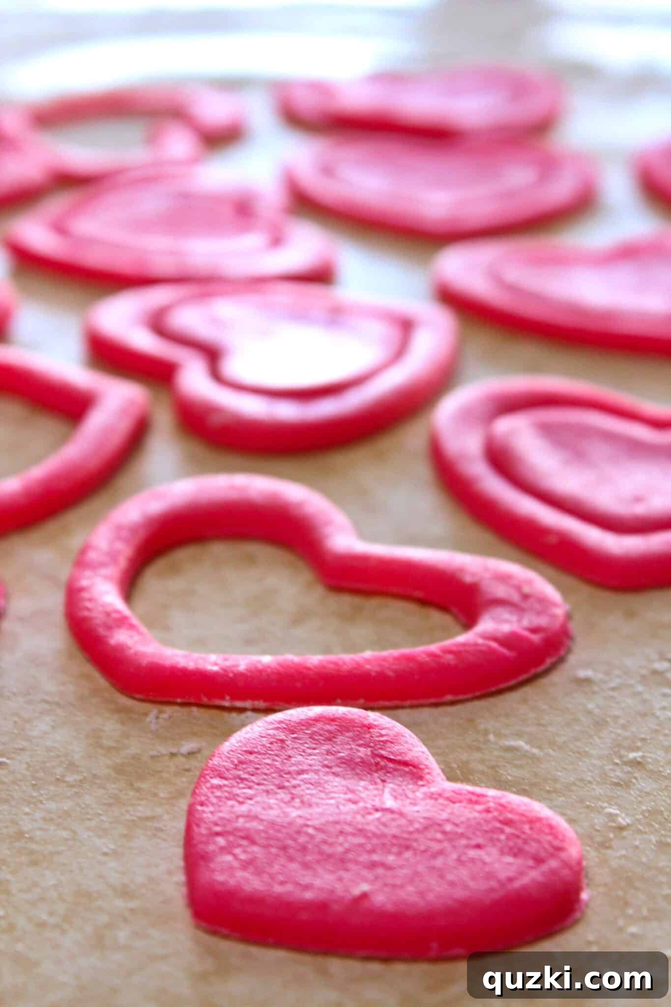 Using a smaller heart cookie cutter to remove the center from a pink heart cookie, creating a ring
