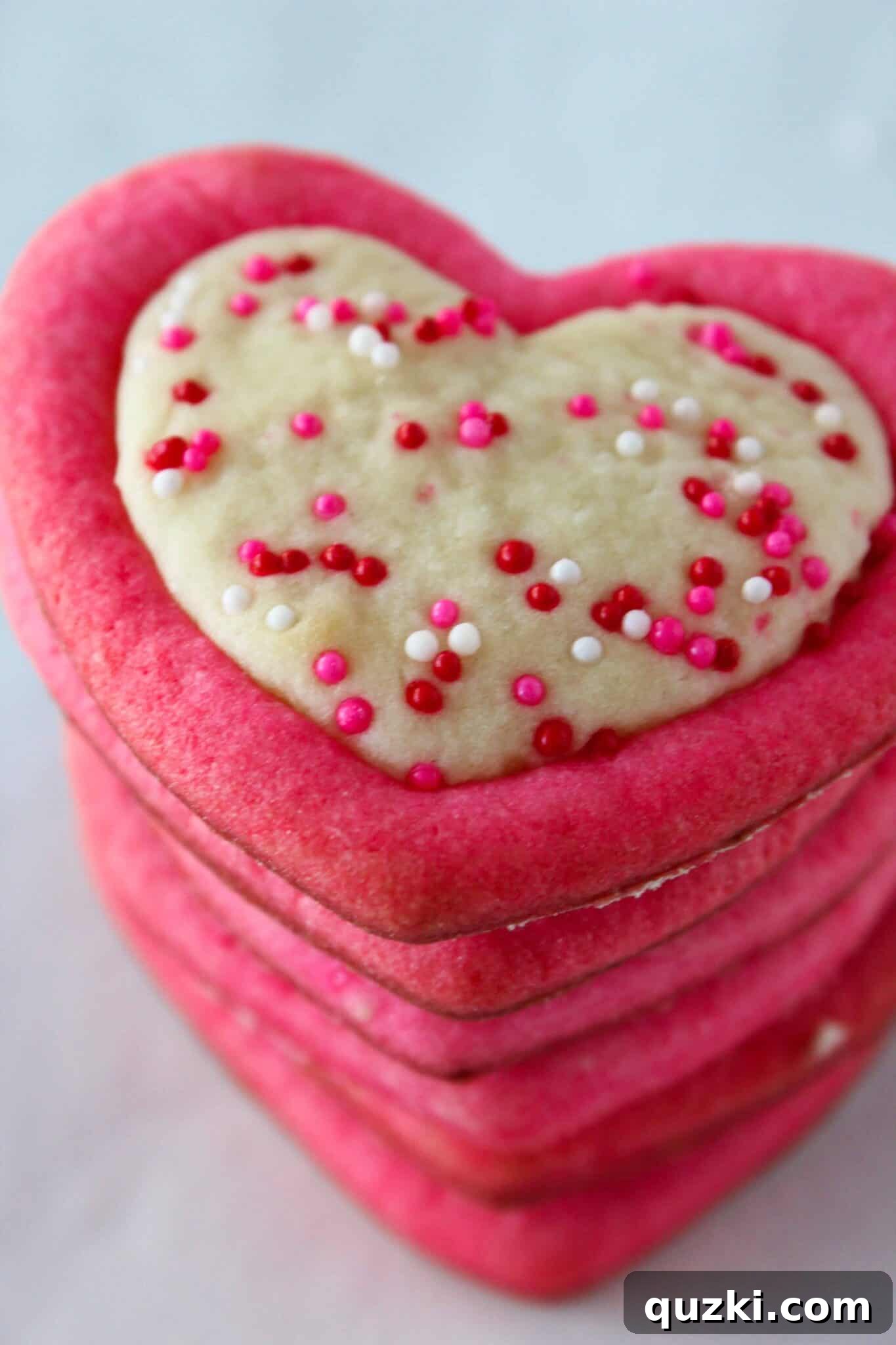 A plate of finished pink sugar cookies with solid pink outlines and sprinkle heart centers
