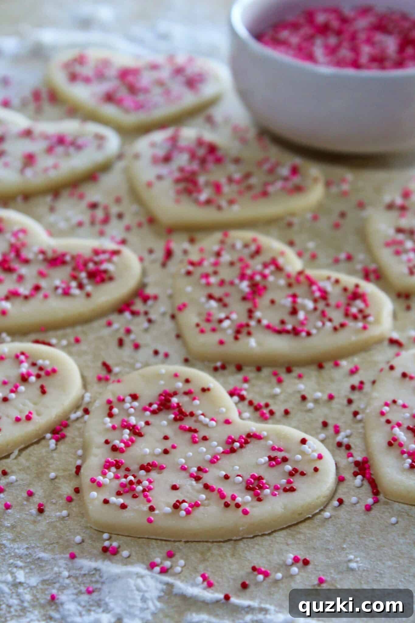 Pressing colorful sprinkles onto the surface of large white heart-shaped cookie dough