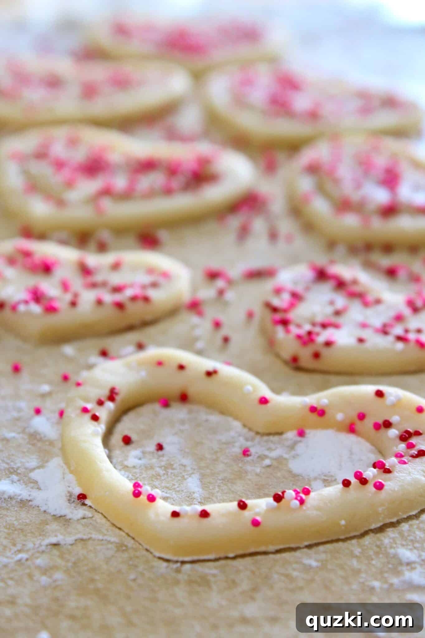 Using a smaller heart cookie cutter to remove the center from a sprinkle-covered white heart cookie